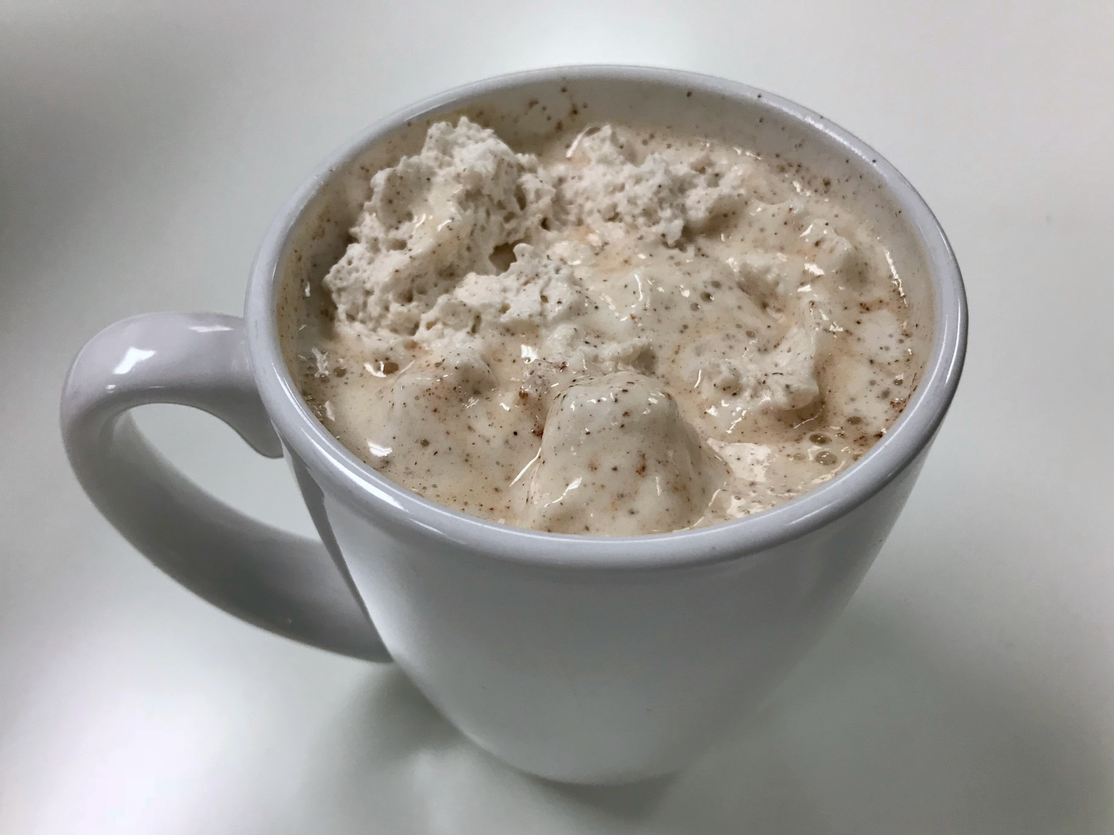 A mug topped with a melty white whipped cream with flecks of spices.