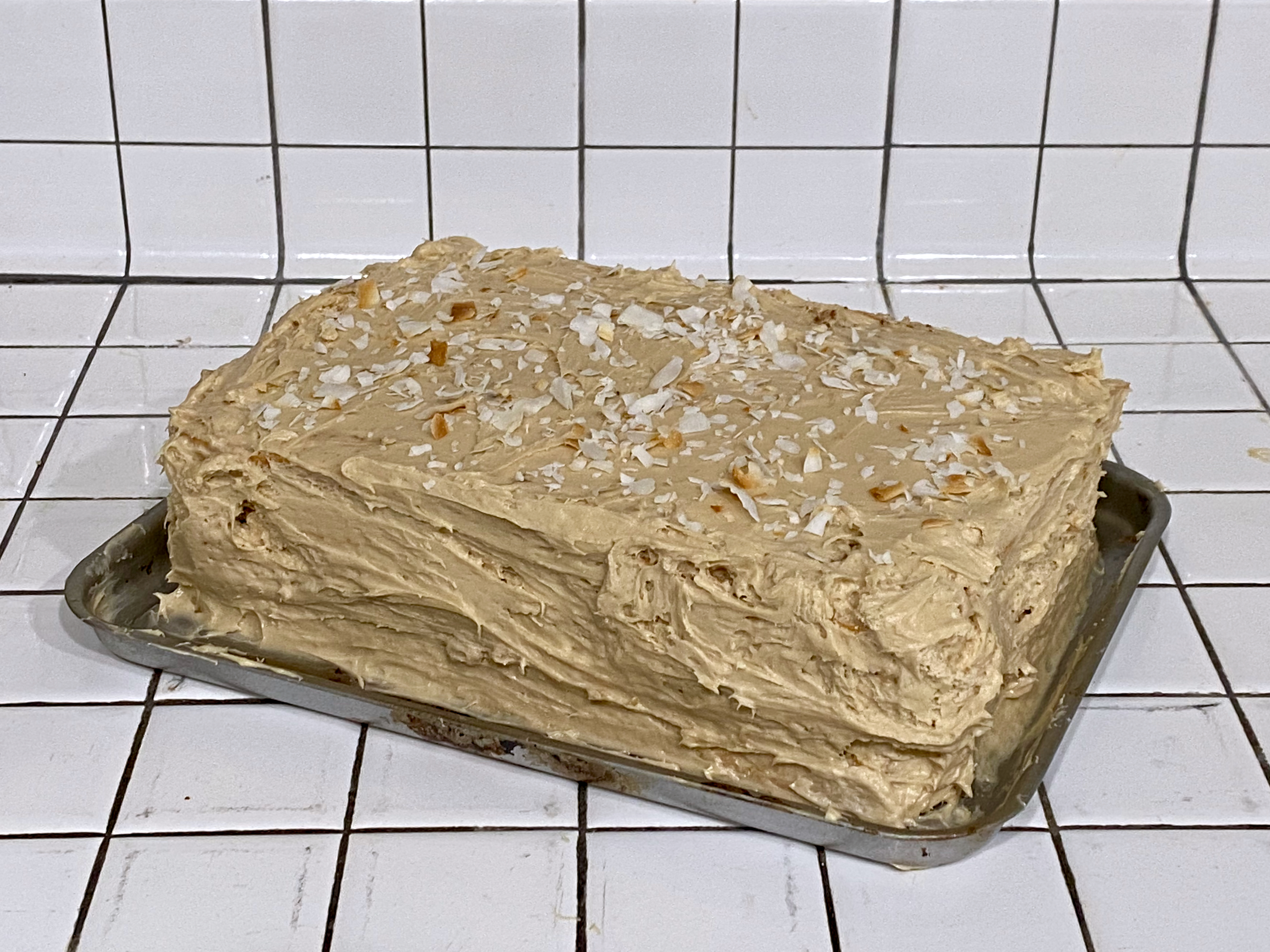 A frosted, coffee-colored two layer cake topped with toasted coconut flakes.