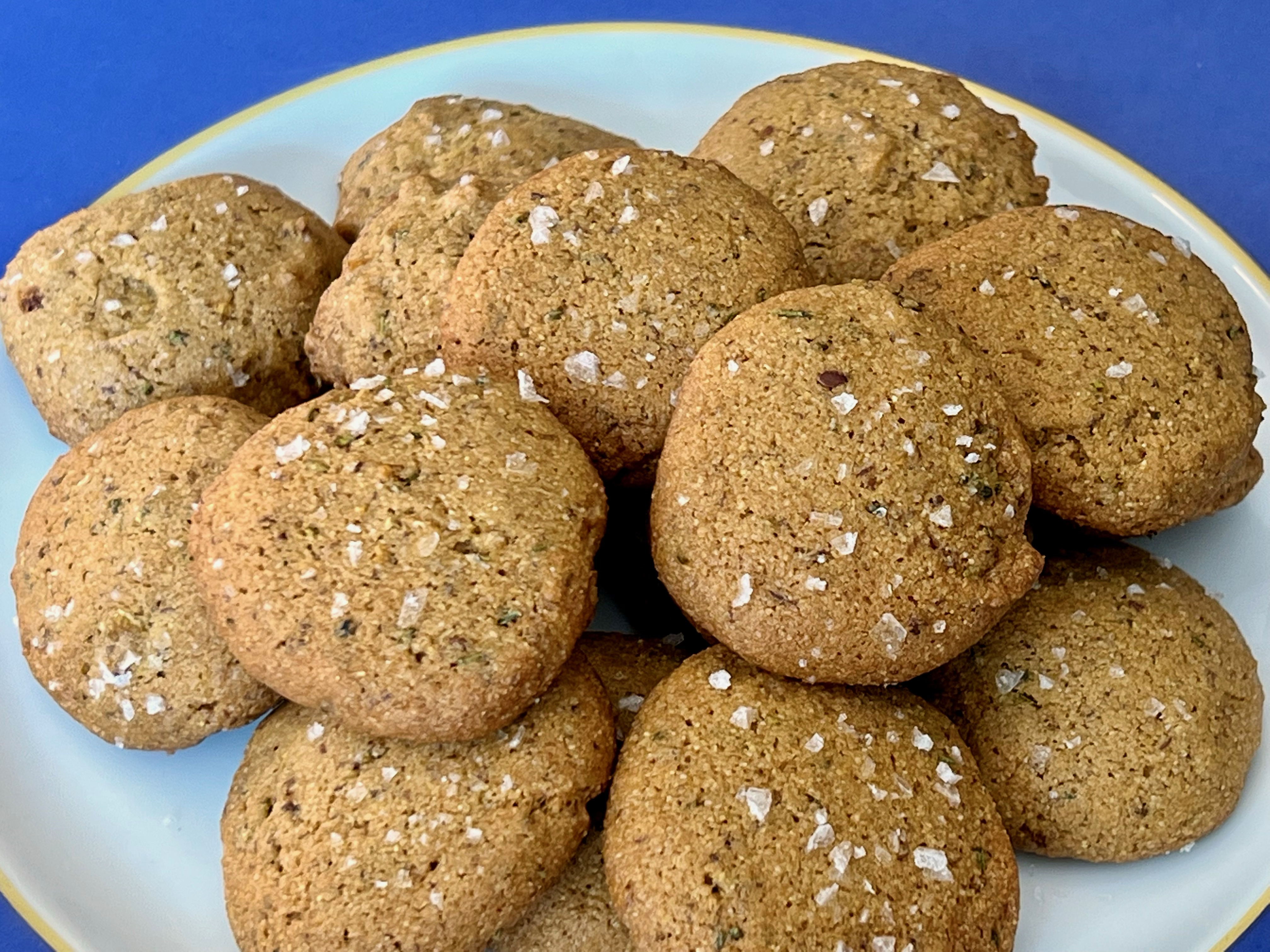 A plate of light brown cookies flecked with green and brown, with flake salt on top.