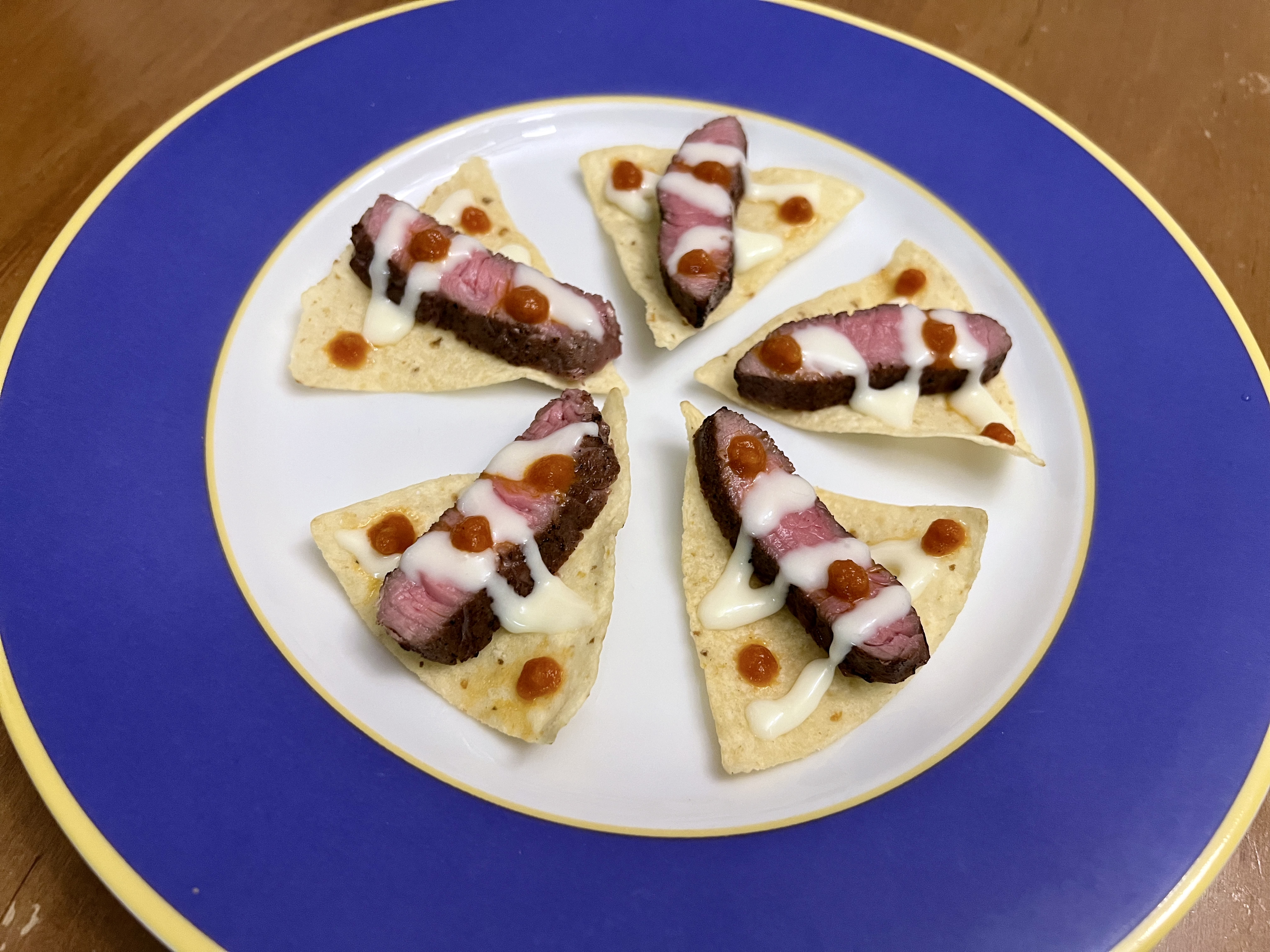 Strips of steak on tortilla chips, topped with a zigzag of white cheese and dotted with red salsa.