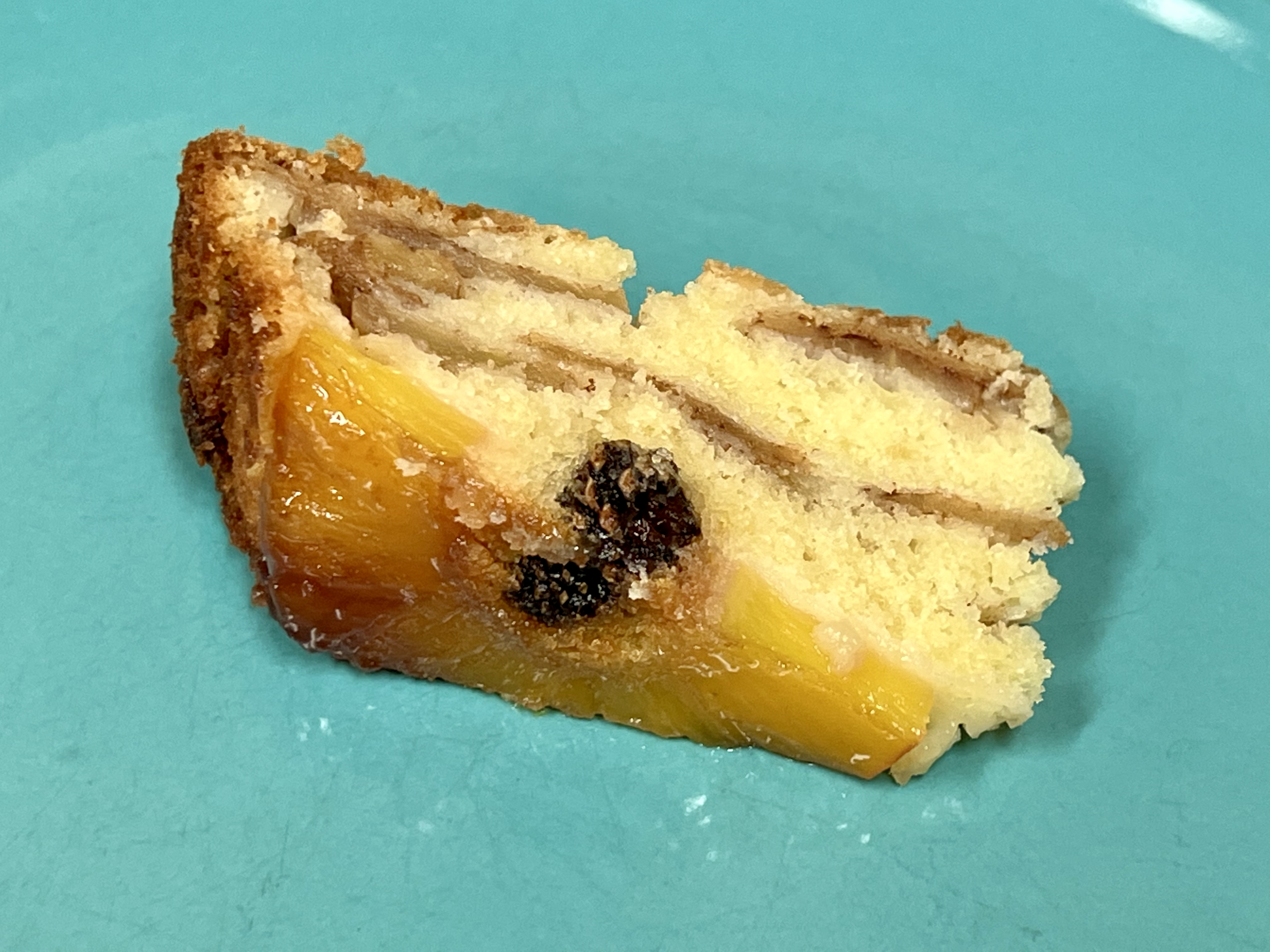 A slice of pineapple upside-down cake with a small pine cone in the pineapple ring and apple slices inside the cake.