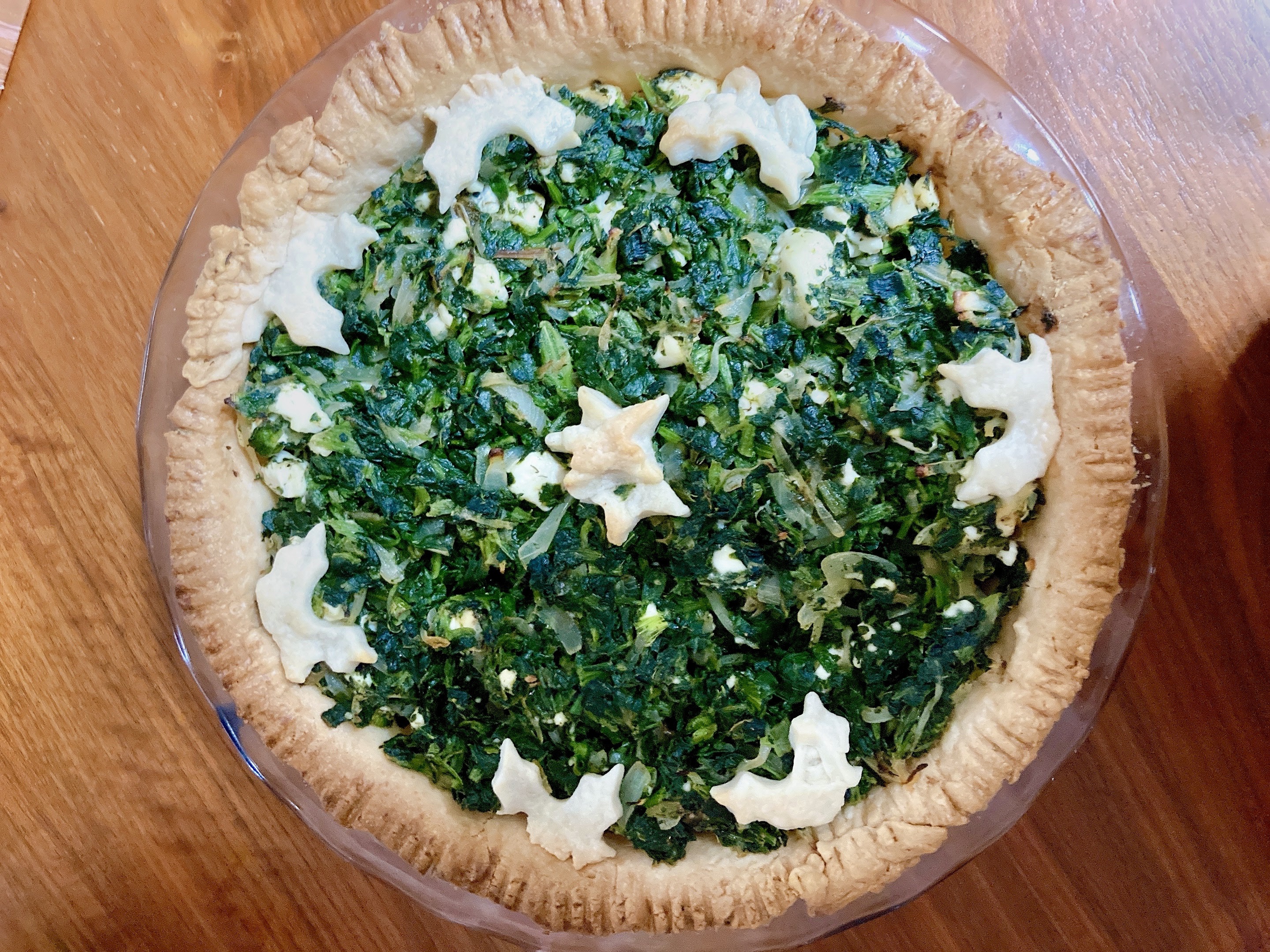 An open topped pie with bright green spinach filling and decorated with pie crust cut into the shapes of leaves.