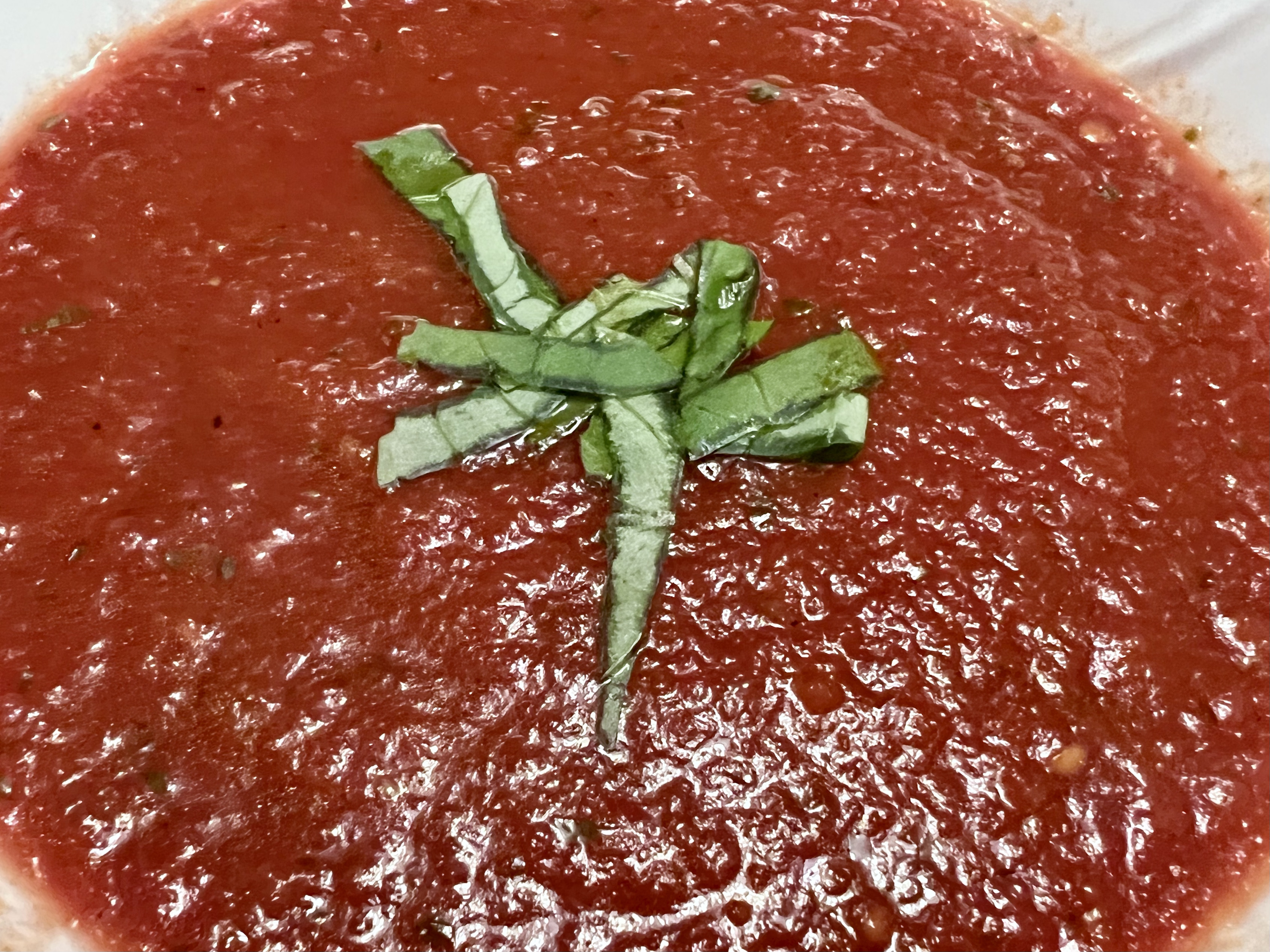 A glistening, deep red tomato soup with flecks of basil within, topped with strips of fresh basil.